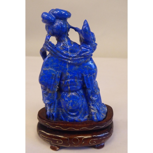 56 - An Oriental carved lapis lazuli kneeling figure, wearing traditional ceremonial costume, holding a l... 