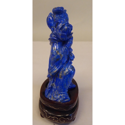 56 - An Oriental carved lapis lazuli kneeling figure, wearing traditional ceremonial costume, holding a l... 