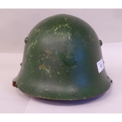 63 - A military design painted steel helmet with a hide liner and buckled chinstrap(Please Note: this lot... 