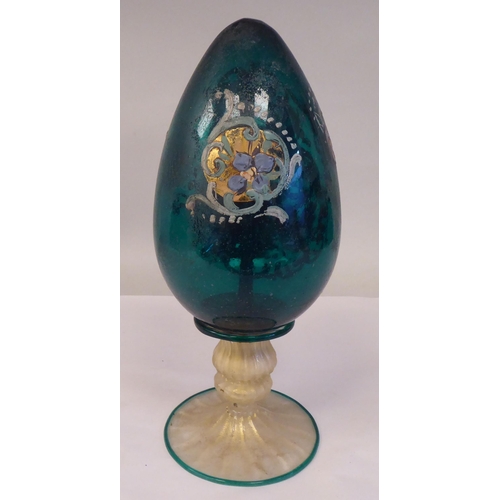 71 - An antique Murano glass two part egg ornament, overpainted and gilded with floral designs, on a semi... 