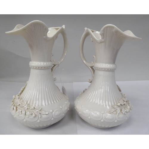 73 - A pair of Belleek pearl ivory glazed porcelain ewers of bulbous form with narrow necks, flared rims,... 