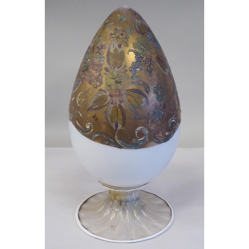 238 - An antique Murano glass two part egg ornament, overpainted and gilded with floral designs, on a whit... 