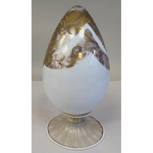 238 - An antique Murano glass two part egg ornament, overpainted and gilded with floral designs, on a whit... 