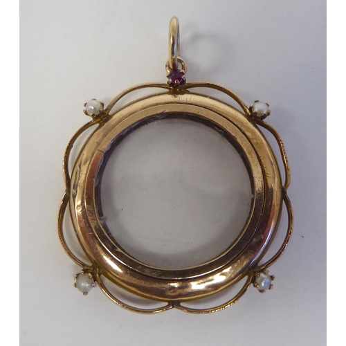 103 - A yellow metal open locket, the glazed circular centre adorned with pearls and a garnet, on a pendan... 