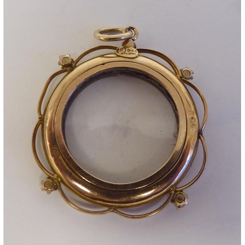 103 - A yellow metal open locket, the glazed circular centre adorned with pearls and a garnet, on a pendan... 