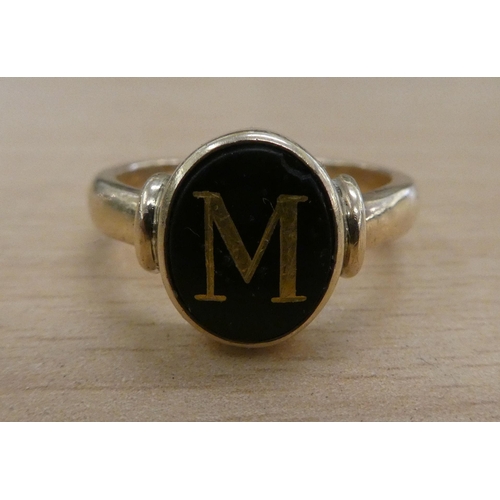 221 - A yellow metal ring, set with a black stone with the letter M  