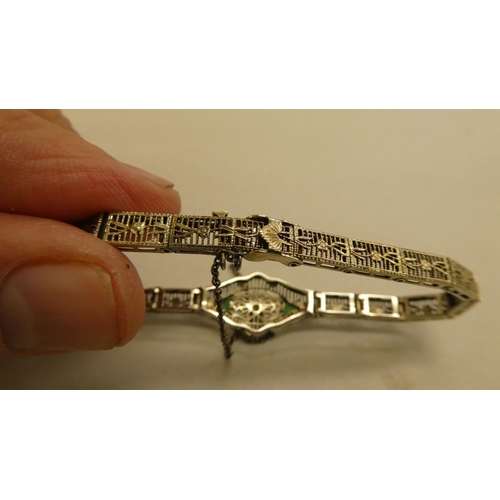 317 - A white metal fine wire hinged bracelet, set with a central diamond and green stones  stamped 14k