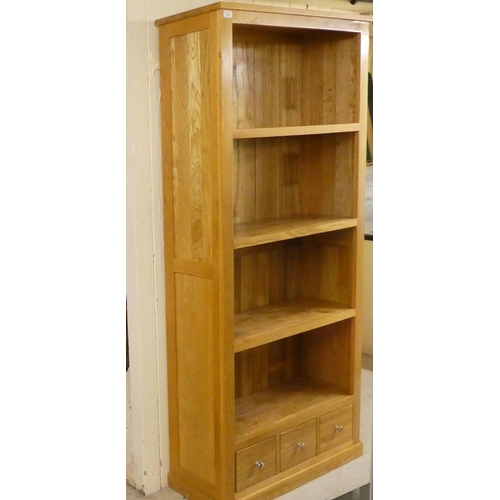 24 - A modern light oak and plywood backed, open front, four tier bookcase with three drawers, on a plint... 