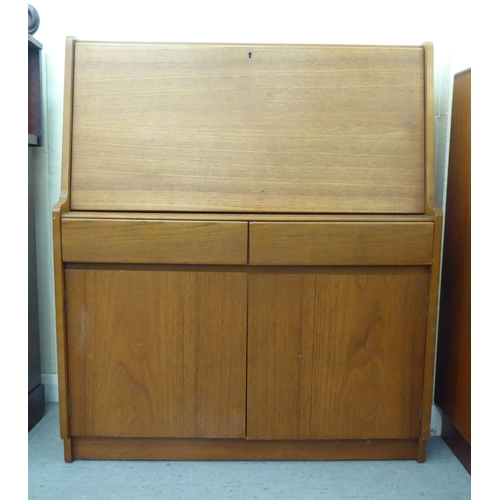 276 - A modern teak bureau, the fall flap enclosing a blotter and pigeon holes, over two drawers and two d... 