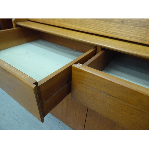 276 - A modern teak bureau, the fall flap enclosing a blotter and pigeon holes, over two drawers and two d... 