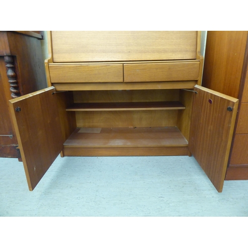 276 - A modern teak bureau, the fall flap enclosing a blotter and pigeon holes, over two drawers and two d... 