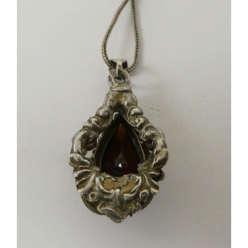 81 - A white metal pendant, set with a teardrop cut garnet, on a white metal chain  stamped 800