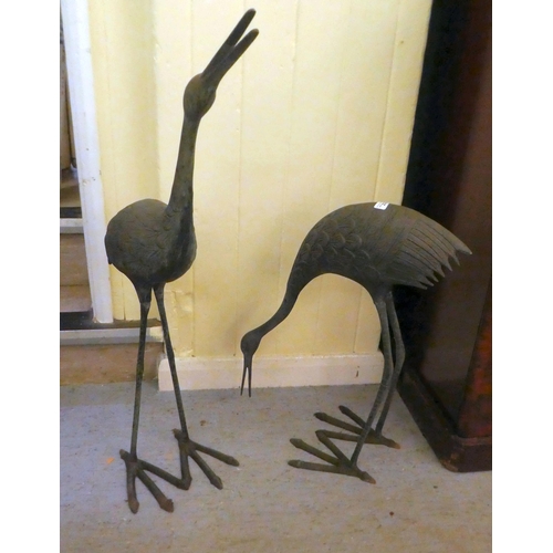 223 - Two patinated cast metal garden ornaments, standing cranes  24