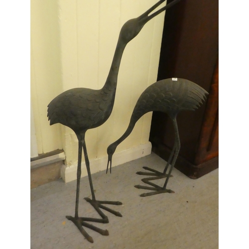 223 - Two patinated cast metal garden ornaments, standing cranes  24