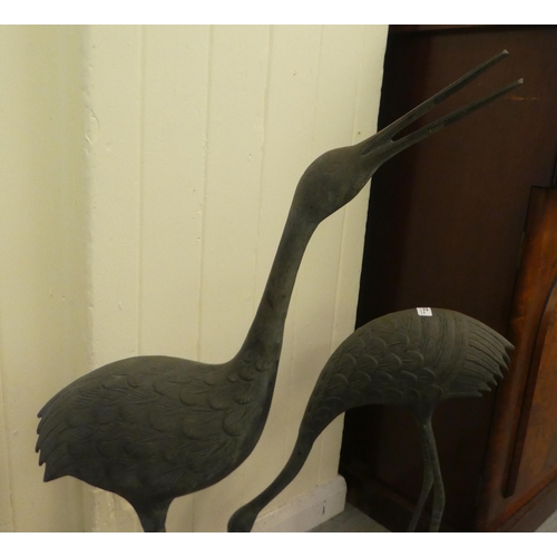 223 - Two patinated cast metal garden ornaments, standing cranes  24