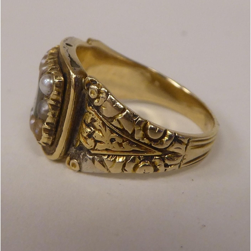 252 - An antique gold coloured metal mourning ring with an engraved shank, set with seed pearls 