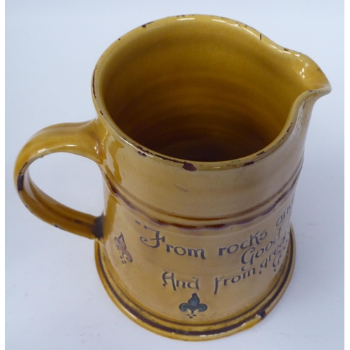 62 - A West Country yellow glazed pottery ale jug of tapered form, inscribed  'From rocks and Lands and B... 