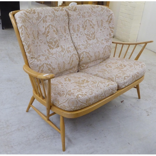 69 - An Ercol blonde beech and elm framed settee with a spindled, level back and open arms, raised on ell... 