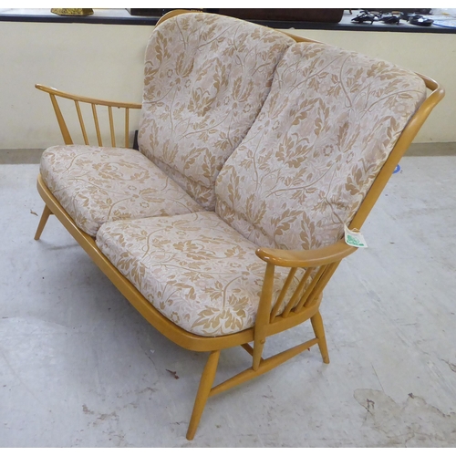 69 - An Ercol blonde beech and elm framed settee with a spindled, level back and open arms, raised on ell... 