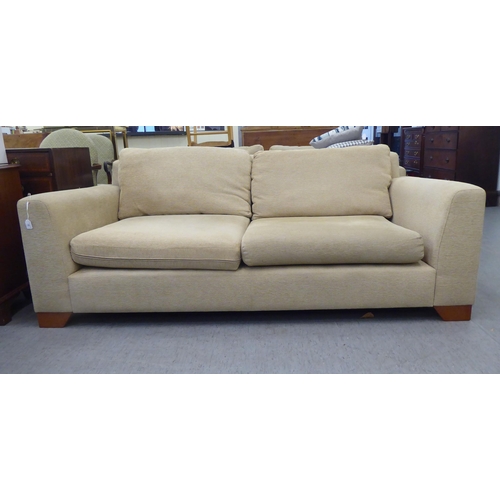 72 - A modern two person settee, upholstered in oatmeal coloured fabric with a level back and arms, raise... 