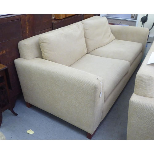 71 - A modern two person settee, upholstered in oatmeal coloured fabric with a level back and arms, raise... 