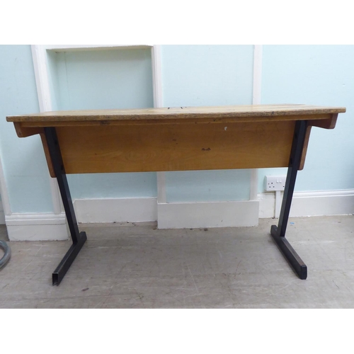 214 - A mid 20thC two person pine desk with two hinged compartments, raised on cast metal legs  27