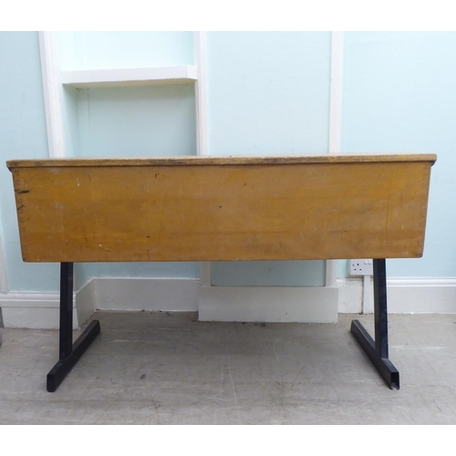 214 - A mid 20thC two person pine desk with two hinged compartments, raised on cast metal legs  27