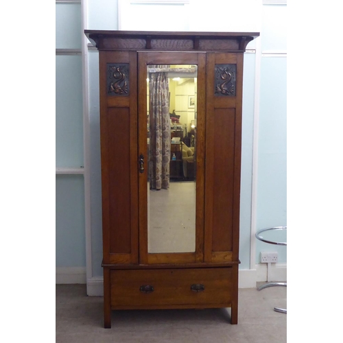 216 - An Arts & Crafts period oak wardrobe with a mirrored door and pressed brass effect panels, over ... 