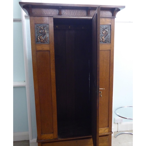 216 - An Arts & Crafts period oak wardrobe with a mirrored door and pressed brass effect panels, over ... 