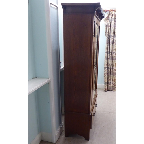 216 - An Arts & Crafts period oak wardrobe with a mirrored door and pressed brass effect panels, over ... 