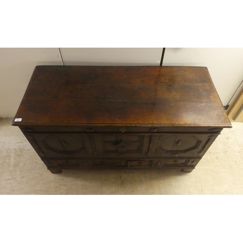 280 - A late 18thC oak coffer with straight sides and a hinged lid, a panelled front and two drawers, rais... 