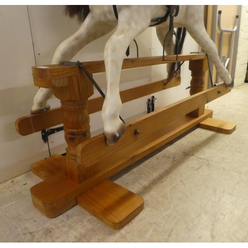 329 - A modern hardwood dapple grey painted rocking horse with a leatherette saddle, raised on a pillar ba... 