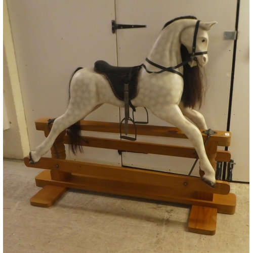 329 - A modern hardwood dapple grey painted rocking horse with a leatherette saddle, raised on a pillar ba... 