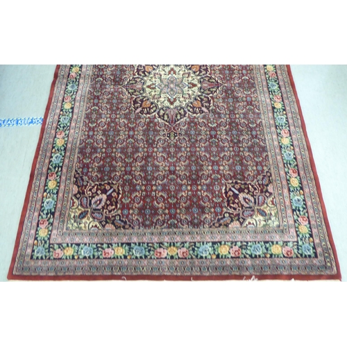 102 - An Indian rug, profusely decorated with repeating floral and other stylised designs, on a mainly red... 