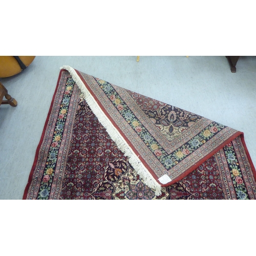 102 - An Indian rug, profusely decorated with repeating floral and other stylised designs, on a mainly red... 