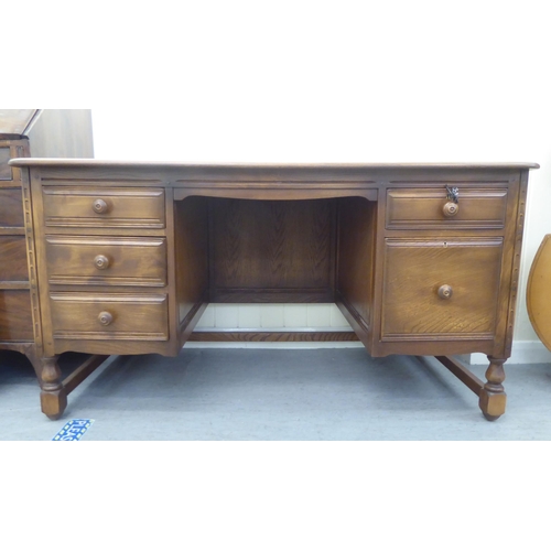 325 - An Ercol mid brown beech and elm framed panelled, twin pedestal, kneehole desk, comprising an arrang... 