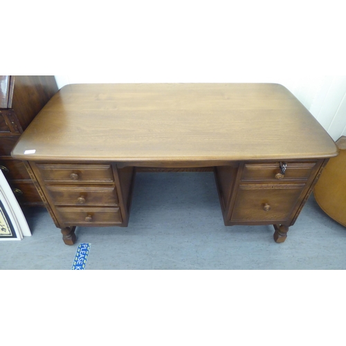 325 - An Ercol mid brown beech and elm framed panelled, twin pedestal, kneehole desk, comprising an arrang... 