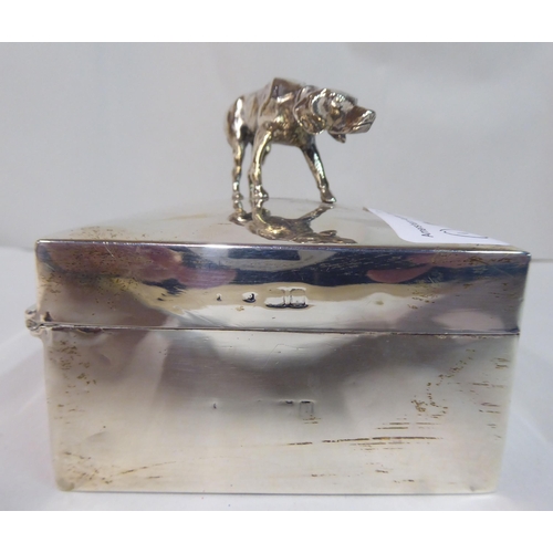 34 - A silver cigarette box with straight sides and a hinged lid, surmounted by a gun dog finial  London ... 