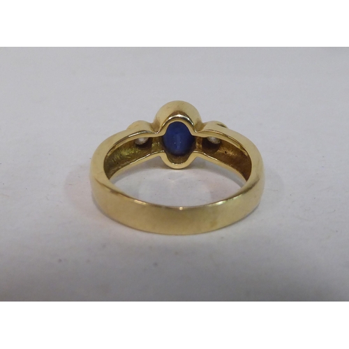 341 - A yellow metal ring, set with a blue stone, flanked by two diamonds