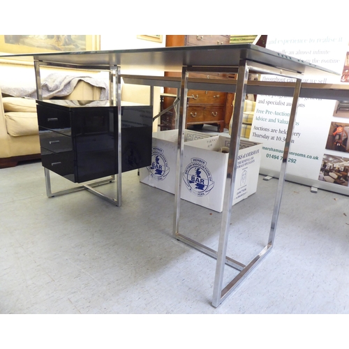 115 - A modern chrome framed, glass top desk with three drawers, raised on rectangular legs  30