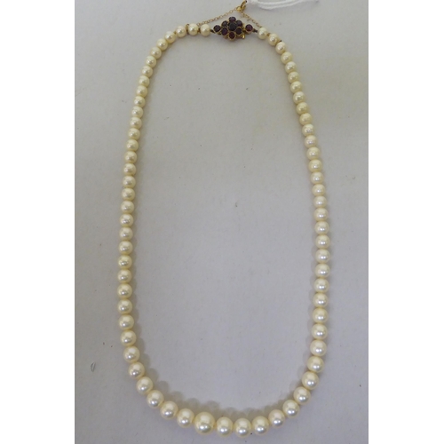 254 - A pearl necklace, on a yellow metal clasp, set with garnets