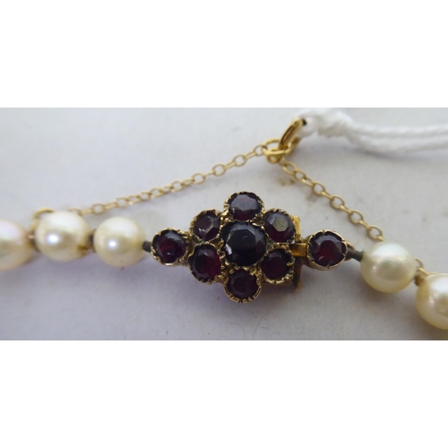 254 - A pearl necklace, on a yellow metal clasp, set with garnets