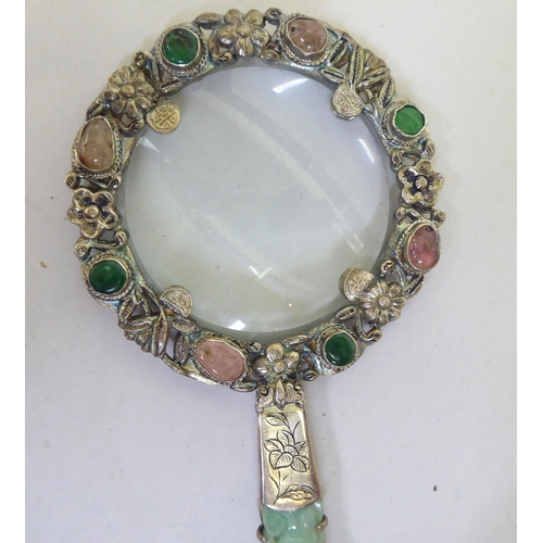 82 - A Chinese white metal magnifying glass set with jade and cabochon cut gems