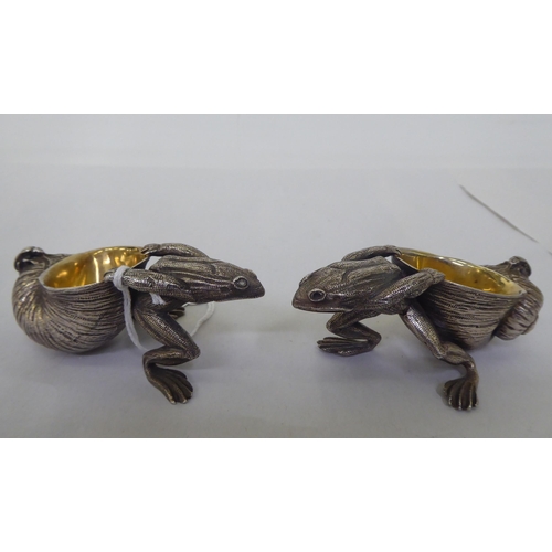 151 - A pair of parcel gilt and white metal novelty salt cellars, each fashioned as a frog, pulling a snai... 