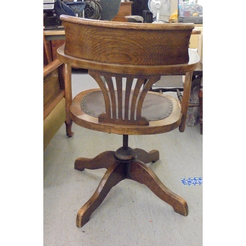 206 - An early 20thC oak framed revolving desk chair, raised on a splayed pedestal base