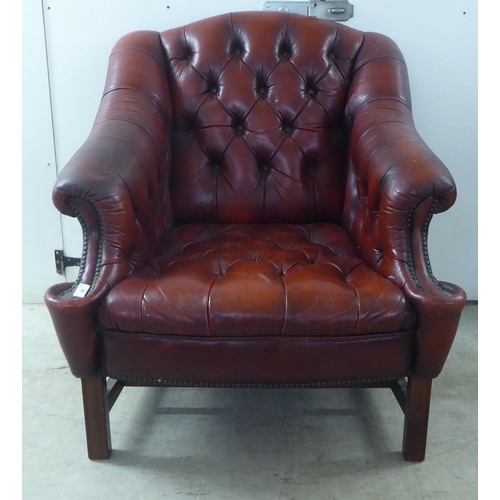 91 - A 20thC buttoned red fabric upholstered enclosed armchair, raised on square forelegs