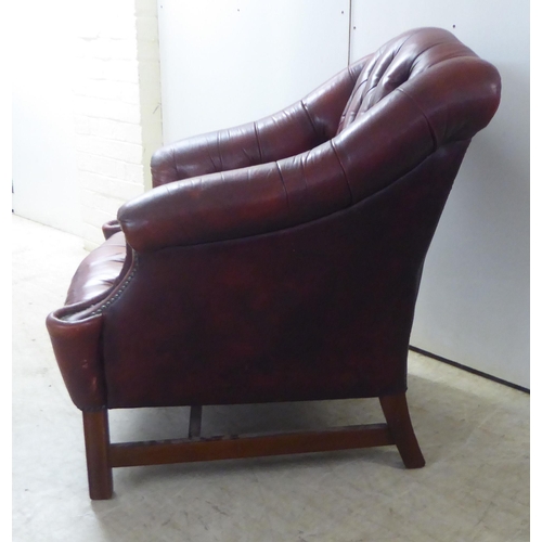 91 - A 20thC buttoned red fabric upholstered enclosed armchair, raised on square forelegs