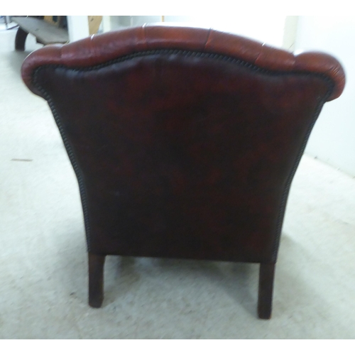 91 - A 20thC buttoned red fabric upholstered enclosed armchair, raised on square forelegs