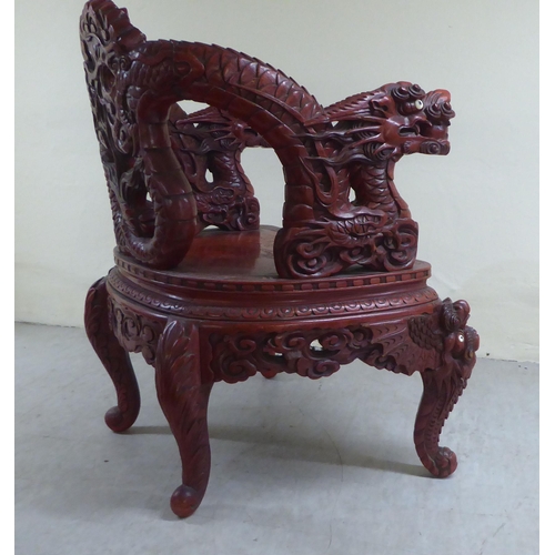 96 - A 20thC Sino-European red stained and profusely carved round back chair, featuring entwined dragons,... 