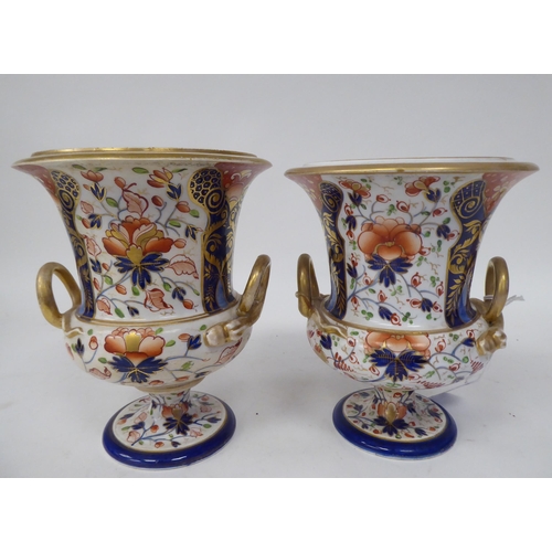 254 - A pair of early 19thC Derby porcelain, twin handled, pedestal urns, decorated in a version of an Ima... 